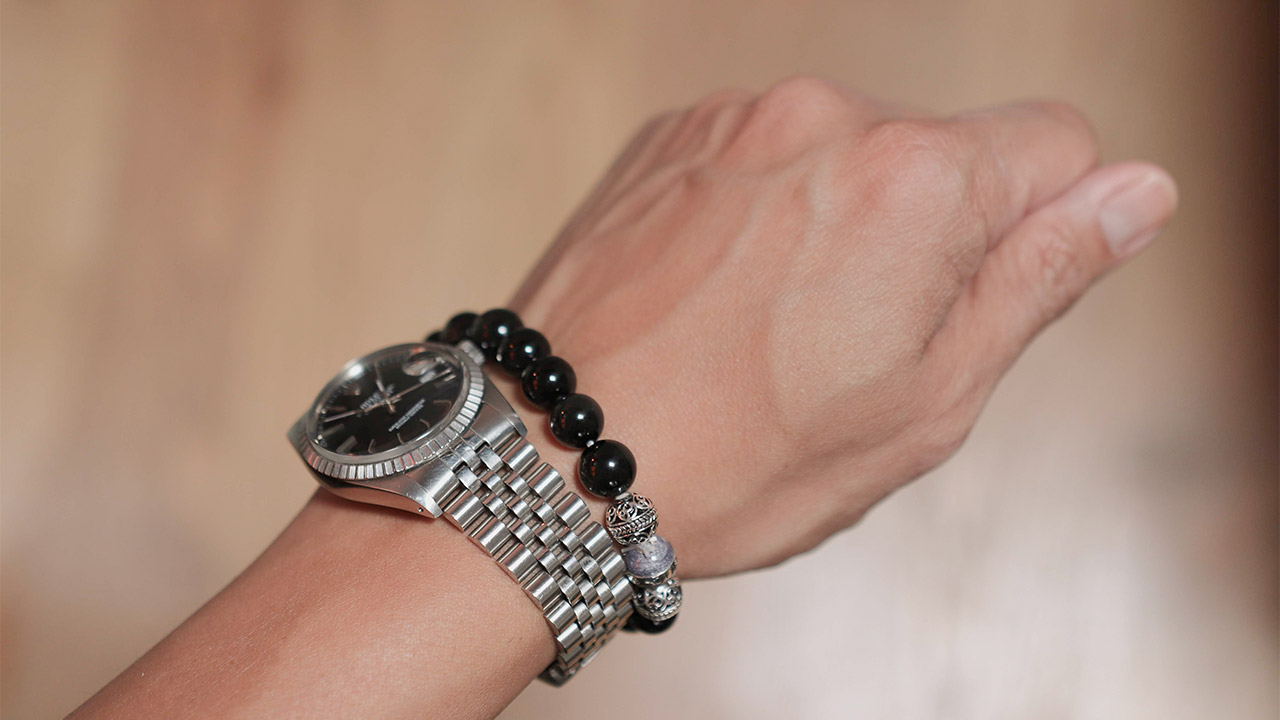 closeup of man's wrist wearing steel rolex datejust watch and beaded bracelet