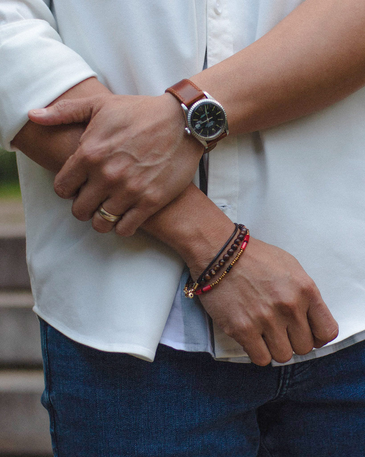 close up image of man holding elbow with a watch on one wrist and bracelets on the other 