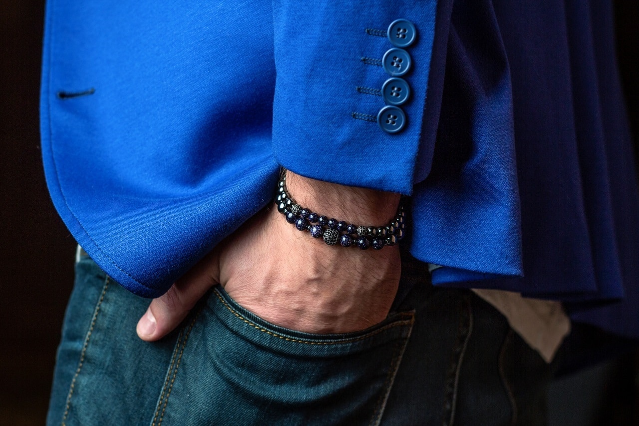 closeup of beaded bracelets on wrist of man wearing blue blazer