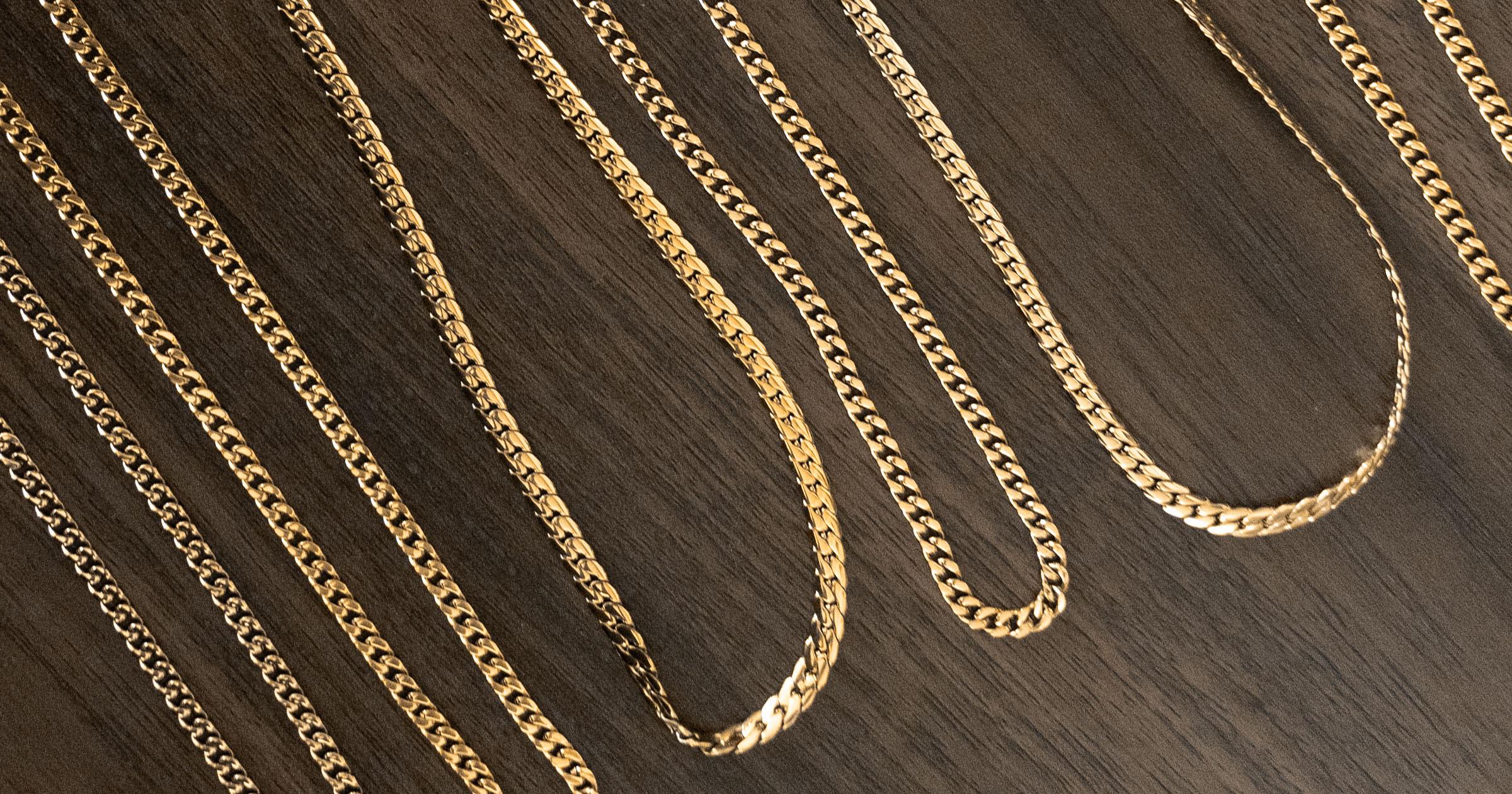 closeup of various solid and hollow gold chains laid out on a wood table